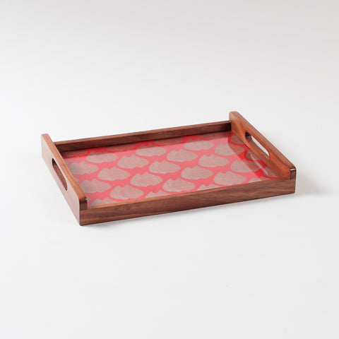 Angled view of a wooden serving tray with red chanderi fabric and golden paisley pattern under glass surface