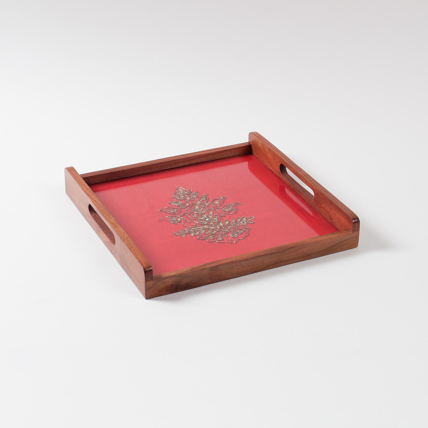 Angled view of a handcrafted wooden serving tray with red and golden paisley gota patti design and glass topping on sheesham wood base