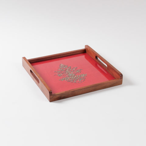 Angled view of a handcrafted wooden serving tray with red and golden paisley gota patti design and glass topping on sheesham wood base