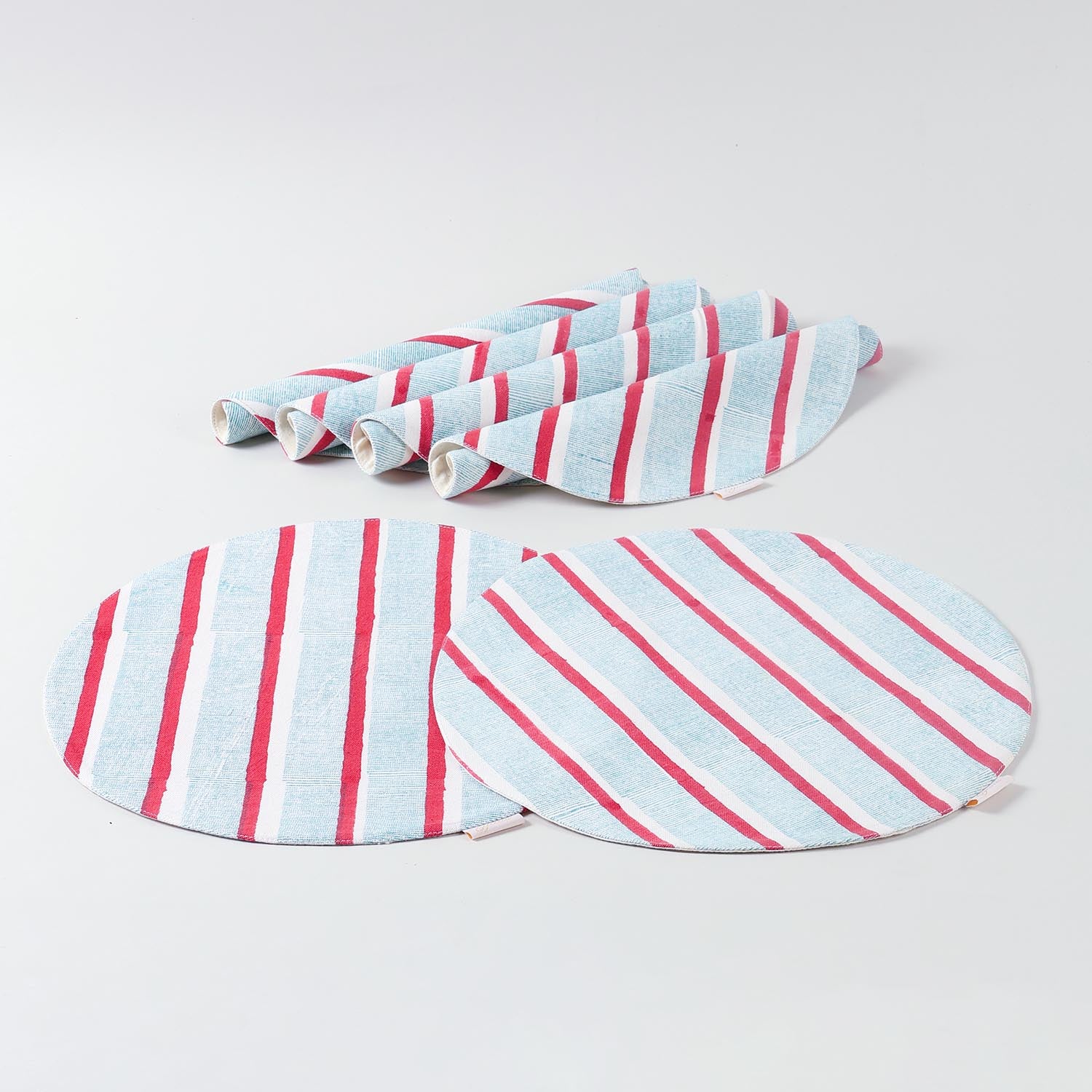 Set of six round cotton placemats with red and green stripe block-printed patterns displayed together on a plain background for dining table settings