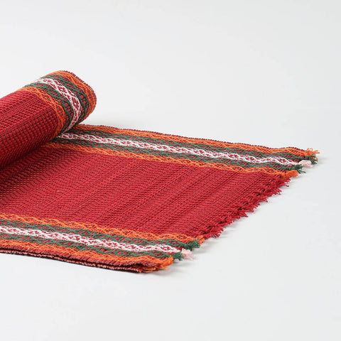 Angled view of a handmade red Madhurkathi table runner showcasing flexible natural fibre weaving and colourful woven borders