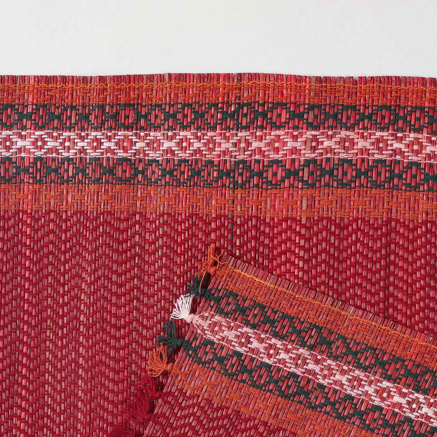 Detailed close-up of a red Madurkathi placemat showcasing the dense natural fibre weave, geometric pattern, and durable stitched border
