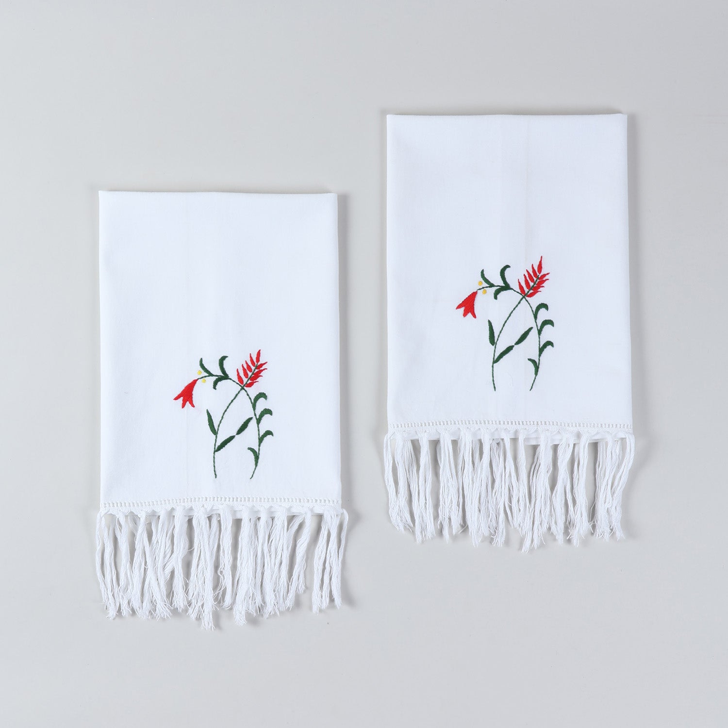 Set of two white cotton kitchen towels featuring red penstemon floral embroidery and tasselled edges