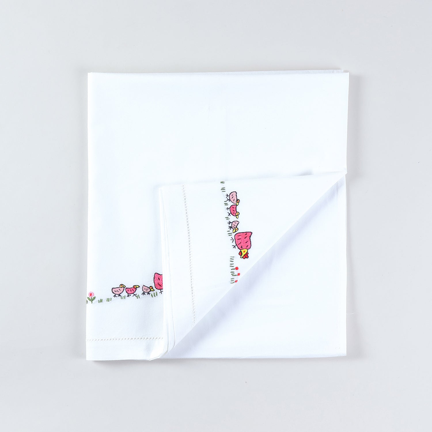 White cotton kids' bedsheet folded back diagonally to showcase colourful rooster embroidery motifs handcrafted on a soft cotton base
