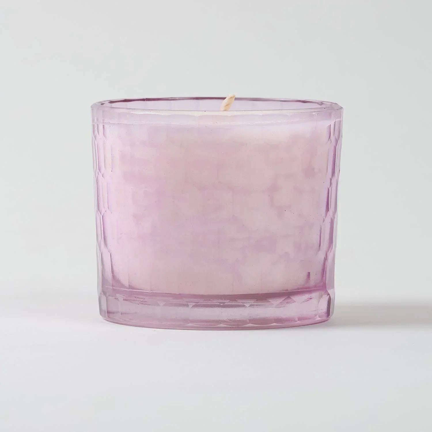 Eye-level view of a rose scented soy wax candle highlighting the textured glass holder and handcrafted finish