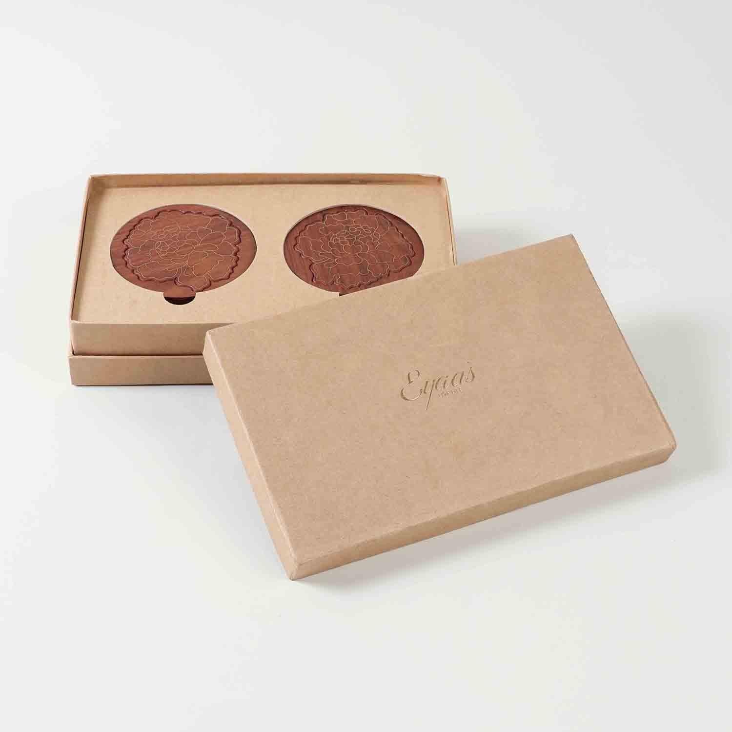Open gift box displaying four rosewood coasters with marigold floral brass inlay, ready for gifting