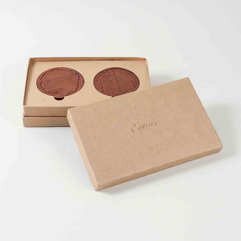 Open gift box displaying four rosewood coasters with marigold floral brass inlay, ready for gifting
