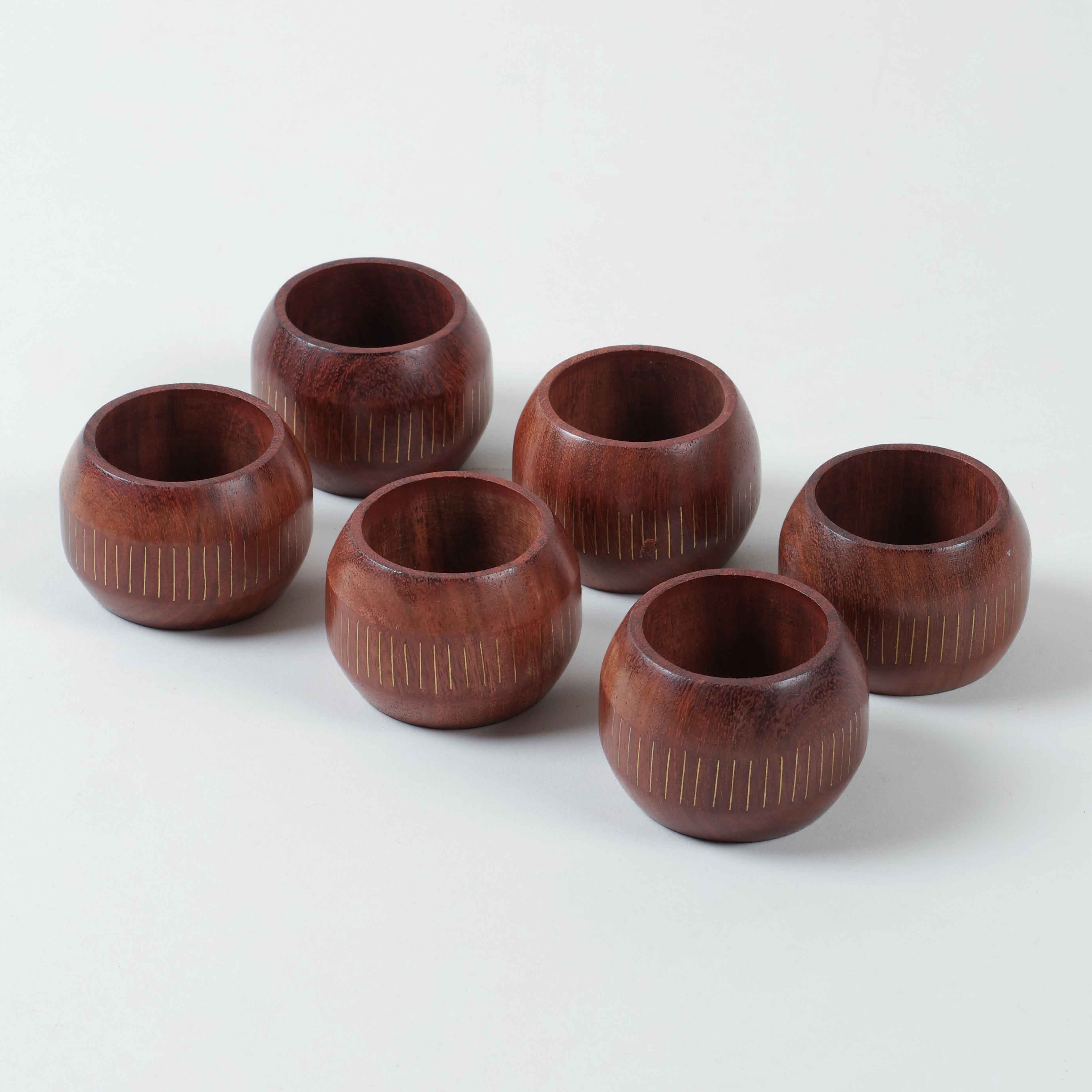 Angled side view of six wooden napkin rings displaying round profiles and decorative brass inlay work