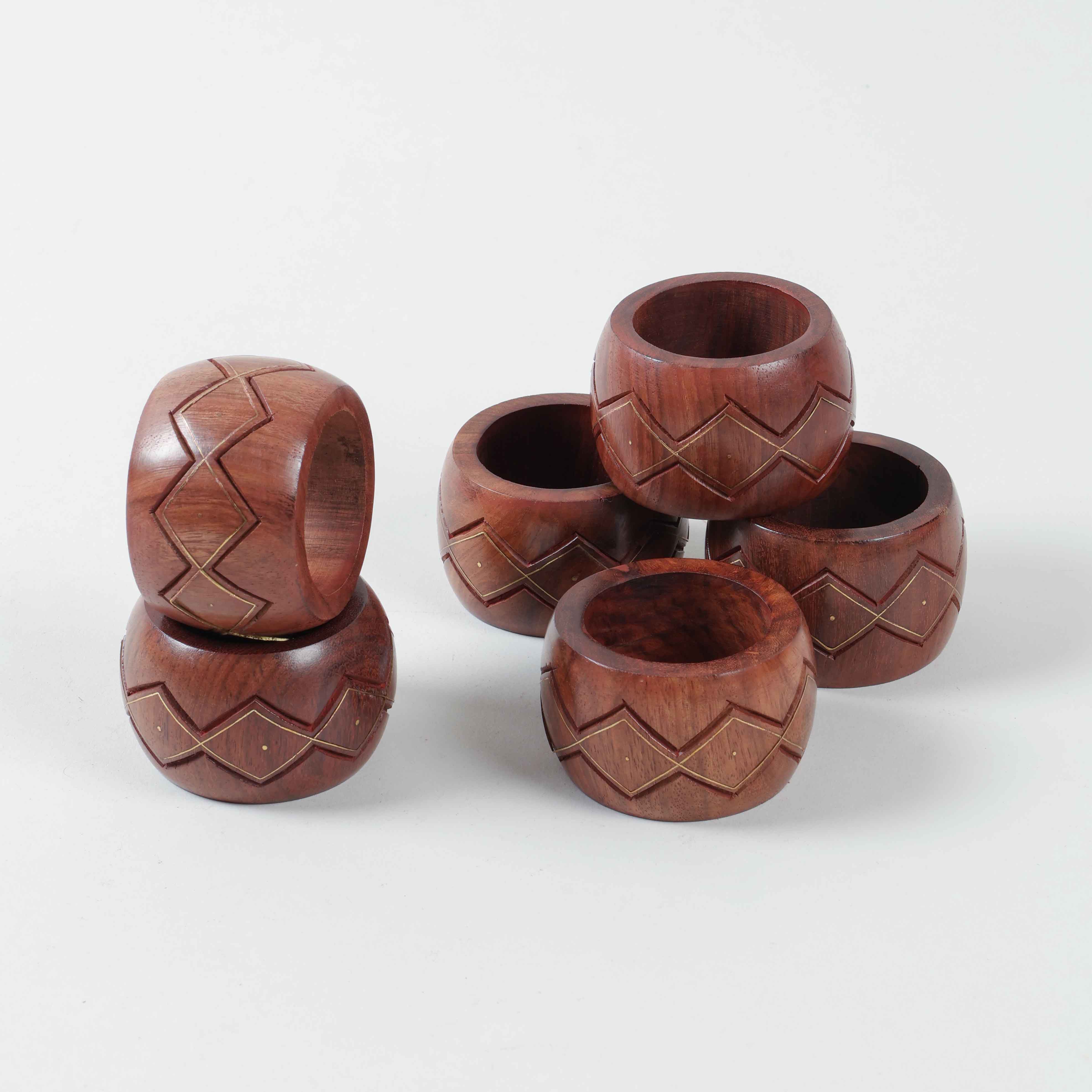 Stacked set of six round wooden napkin rings featuring hand carved zig-zag patterns and decorative brass inlay