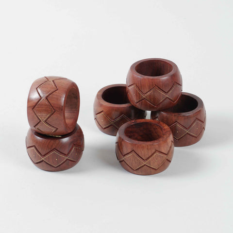 Stacked set of six round wooden napkin rings featuring hand carved zig-zag patterns and decorative brass inlay