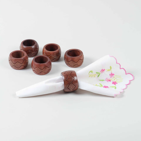 Side view of six round wooden napkin rings highlighting carved texture and brass inlay craftsmanship