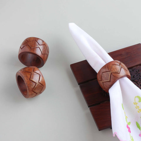 Round wooden napkin rings with zig-zag carving and brass inlay styled on a dining table for elegant table decor