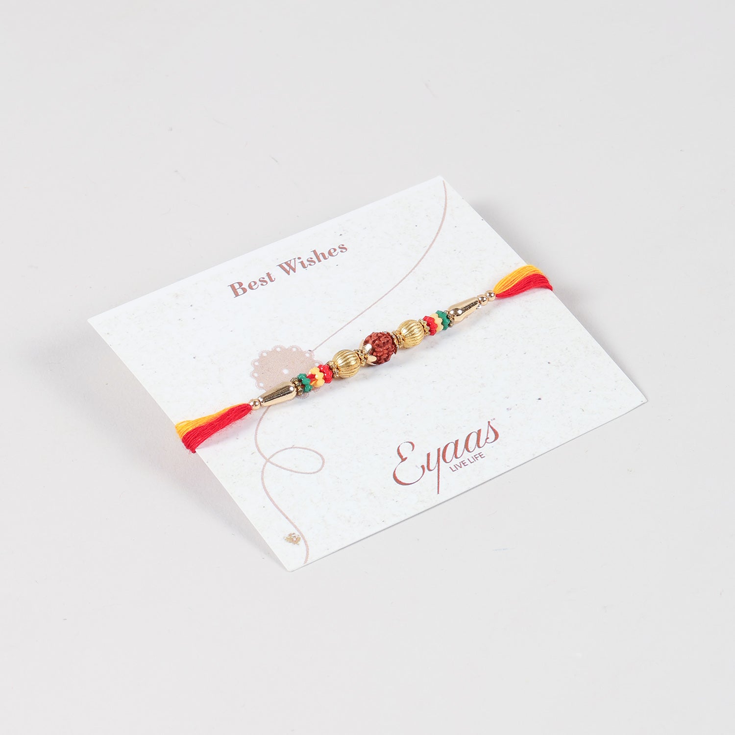 Angled view of the Handmade Rudraksha & Metal Bead Rakhi attached to a Best Wishes greeting card for Raksha Bandhan gifting.
