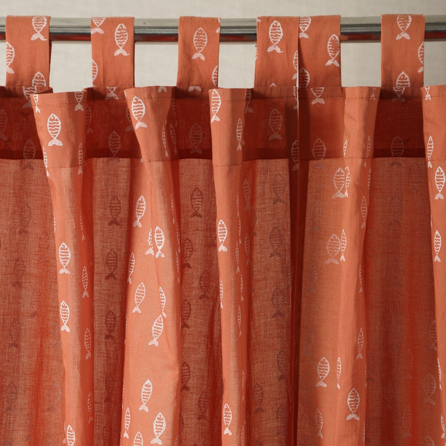 Hand block printed rust mulmul cotton curtain with repeating fish motifs hanging by a window