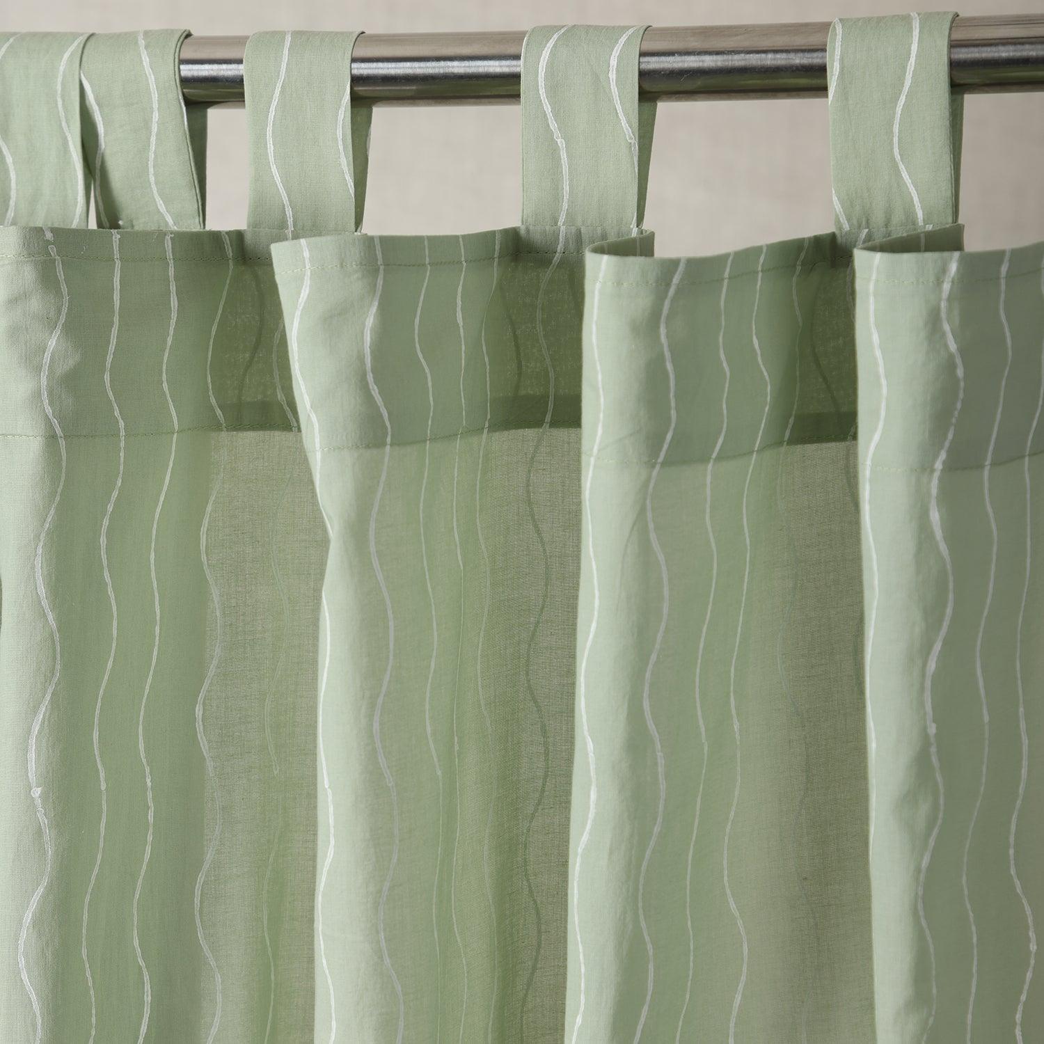 Hand block printed sage green mulmul cotton curtain with a flowing wave pattern hanging by a window
