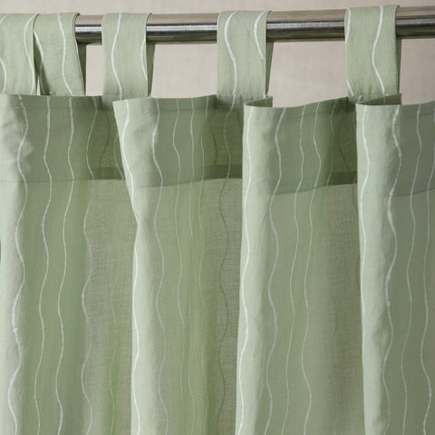 Hand block printed sage green mulmul cotton curtain with a flowing wave pattern hanging by a window