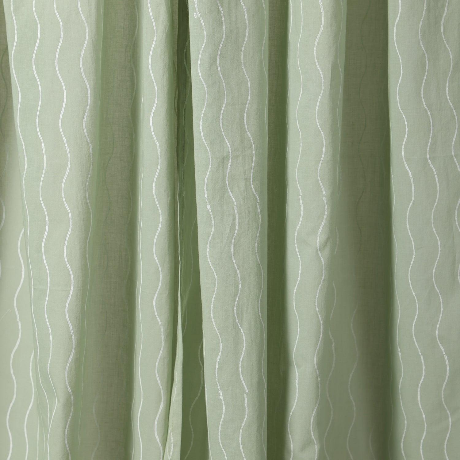 Close-up of the hand block printed wave pattern on soft sage green mulmul cotton curtain fabric.