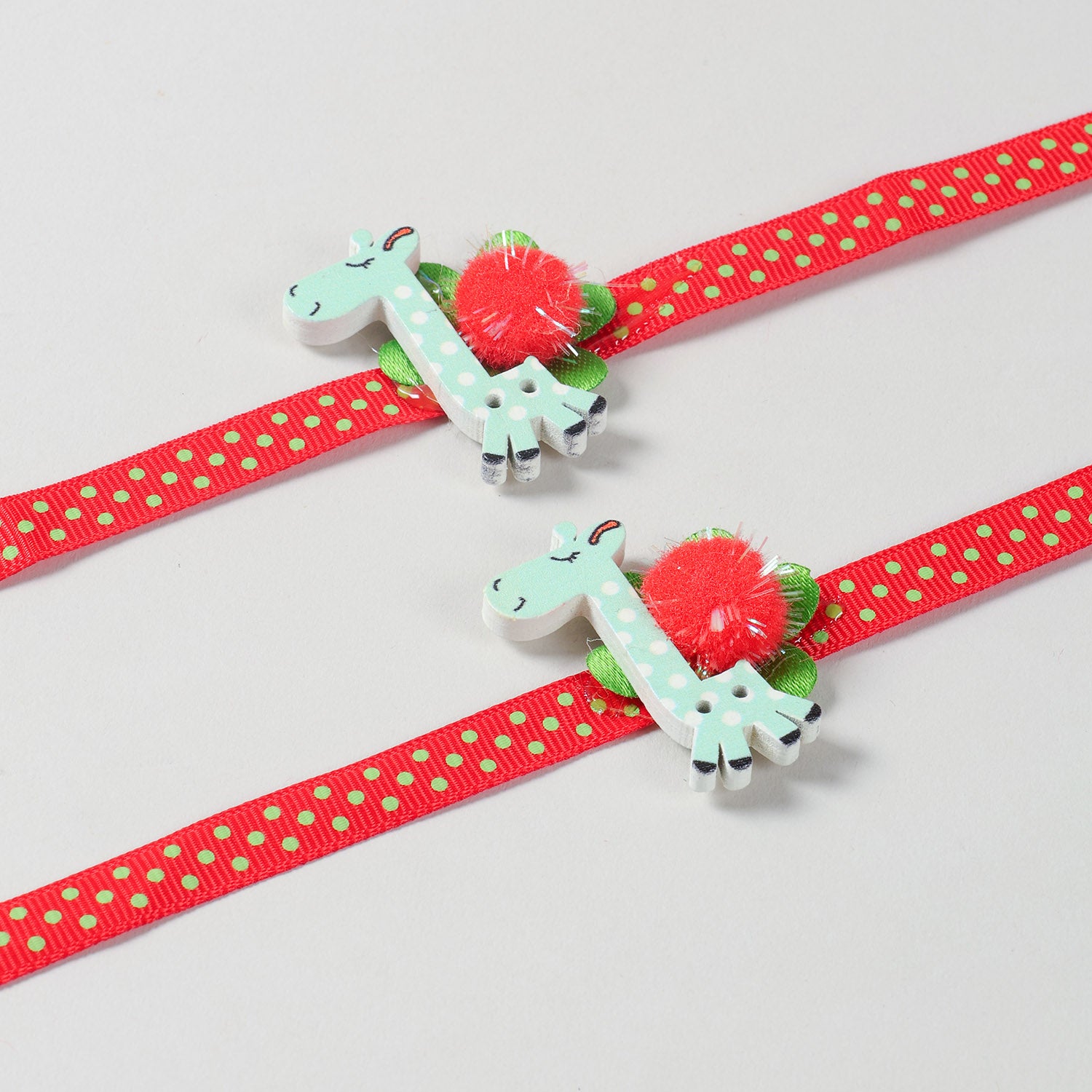 Close-up of the handmade Set of 2 Giraffe Wooden Kids Rakhi with colourful red ribbon and giraffe design.
