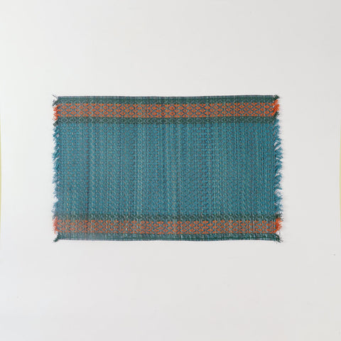 Full view of a handmade blue Madurkathi placemat on a plain background, showcasing natural river grass weaving and colourful border detailing