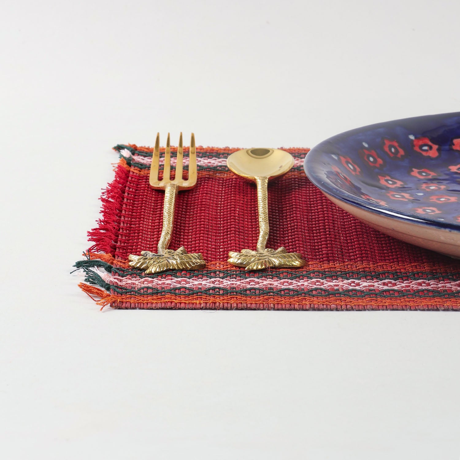 Handmade red Madurkathi placemat styled on a dining table with tableware, showcasing natural fibre texture and elegant table setting