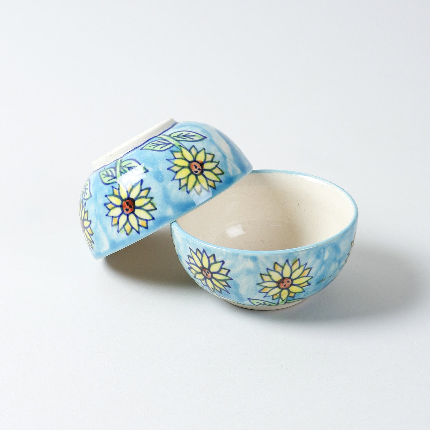 Hand-painted Sunflower ceramic katori set with one bowl upright and another resting upside down at an angle, highlighting handcrafted Khurja ceramic detailing