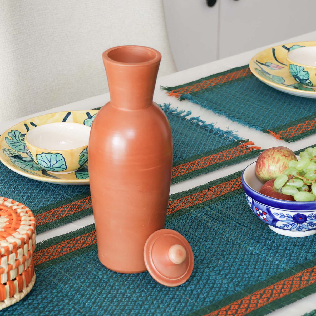 Handmade terracotta water bottle with lid styled on a dining table, a sustainable clay bottle for naturally cool drinking water