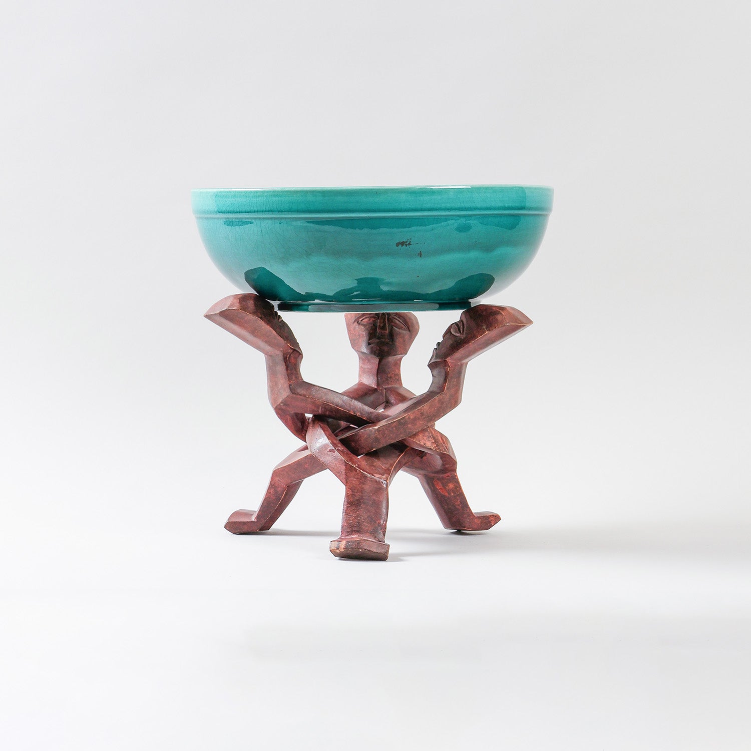 Handmade turquoise ceramic bowl displayed on a carved wooden stand, combining African pottery craftsmanship with functional dining decor