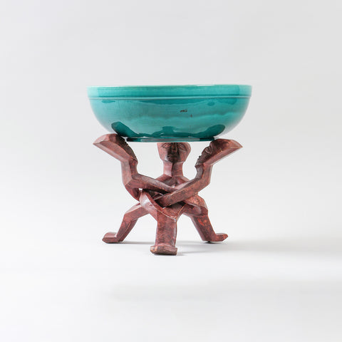 Handmade turquoise ceramic bowl displayed on a carved wooden stand, combining African pottery craftsmanship with functional dining decor