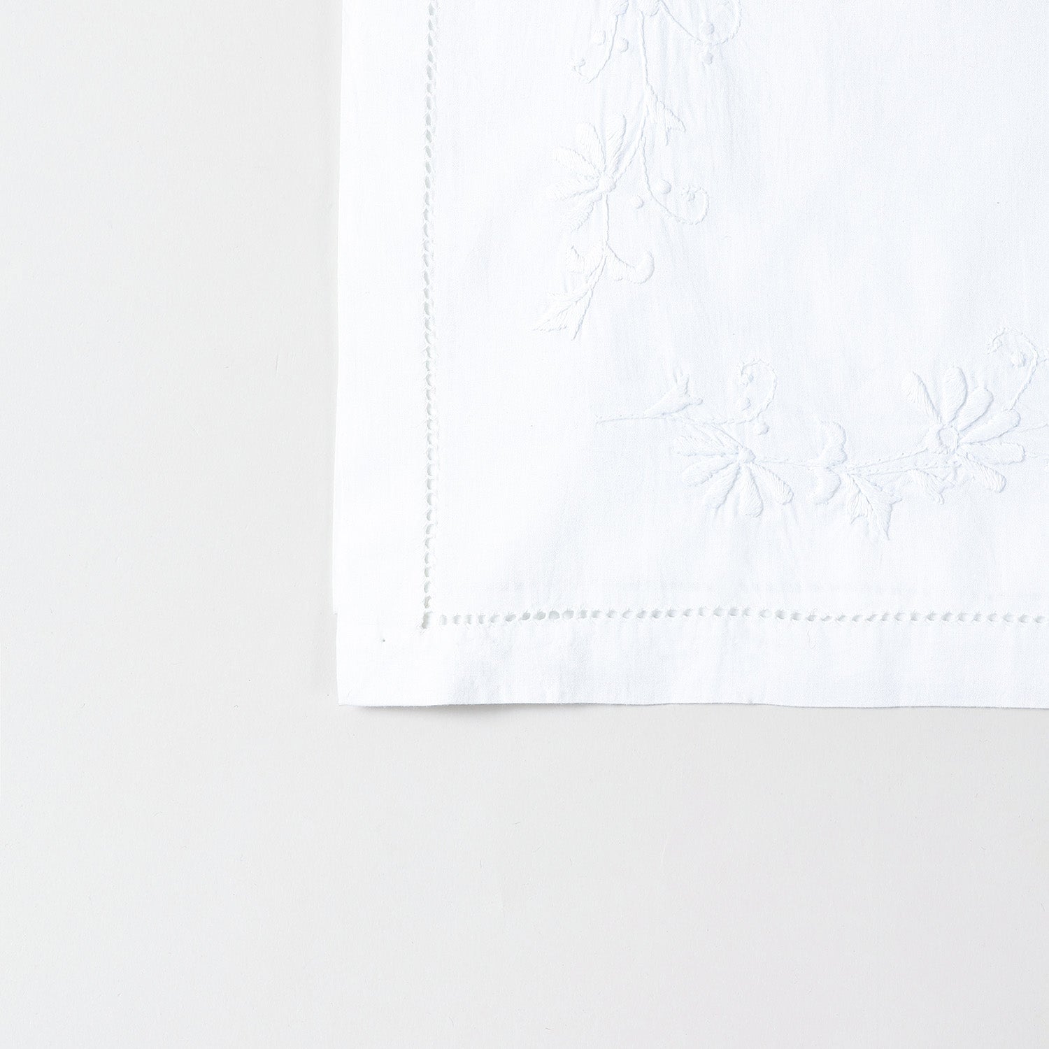 Detailed corner view of a handcrafted table runner featuring elegant white daisy embroidery along the border on a white cotton base