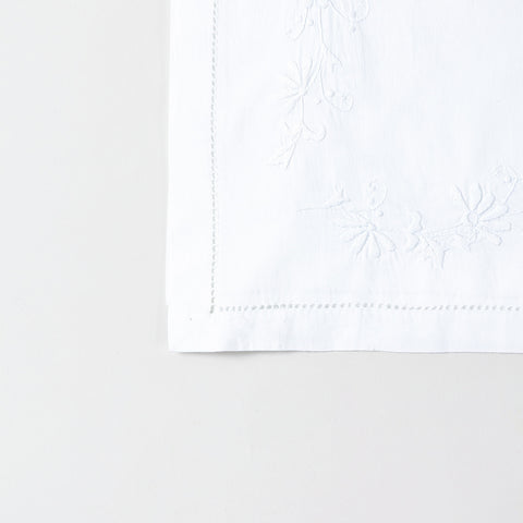 Detailed corner view of a handcrafted table runner featuring elegant white daisy embroidery along the border on a white cotton base