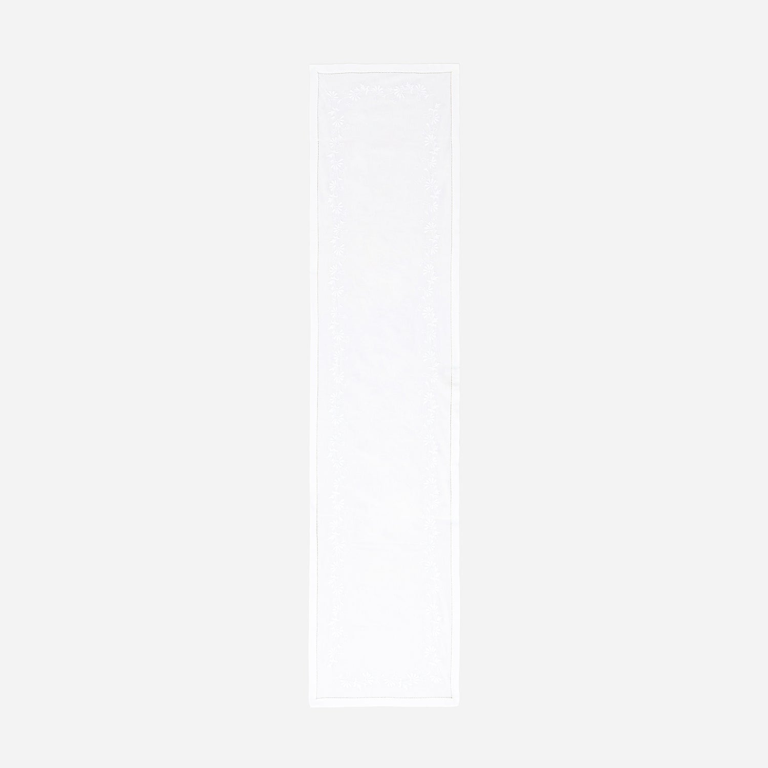 Full-length embroidered table runner featuring white daisy motifs on a white cotton base displayed on a plain background