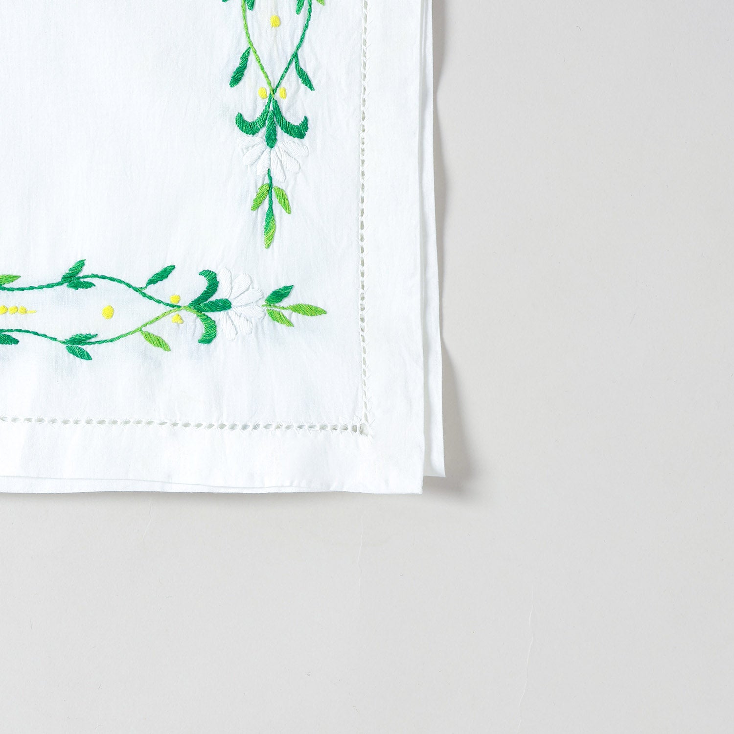 Detailed corner view of a handcrafted embroidered table runner featuring green floral vine embroidery along the border