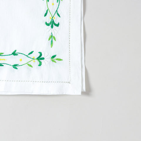 Detailed corner view of a handcrafted embroidered table runner featuring green floral vine embroidery along the border