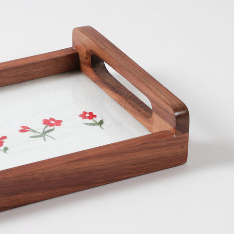 Angled close-up of pink flower embroidery with green leaf details on white cotton fabric used in a handcrafted wooden tray