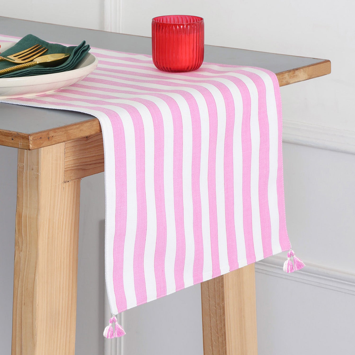 Handwoven cotton table runner with white and pink striped pattern and tassels styled on a dining table, creating a bright and inviting table setting