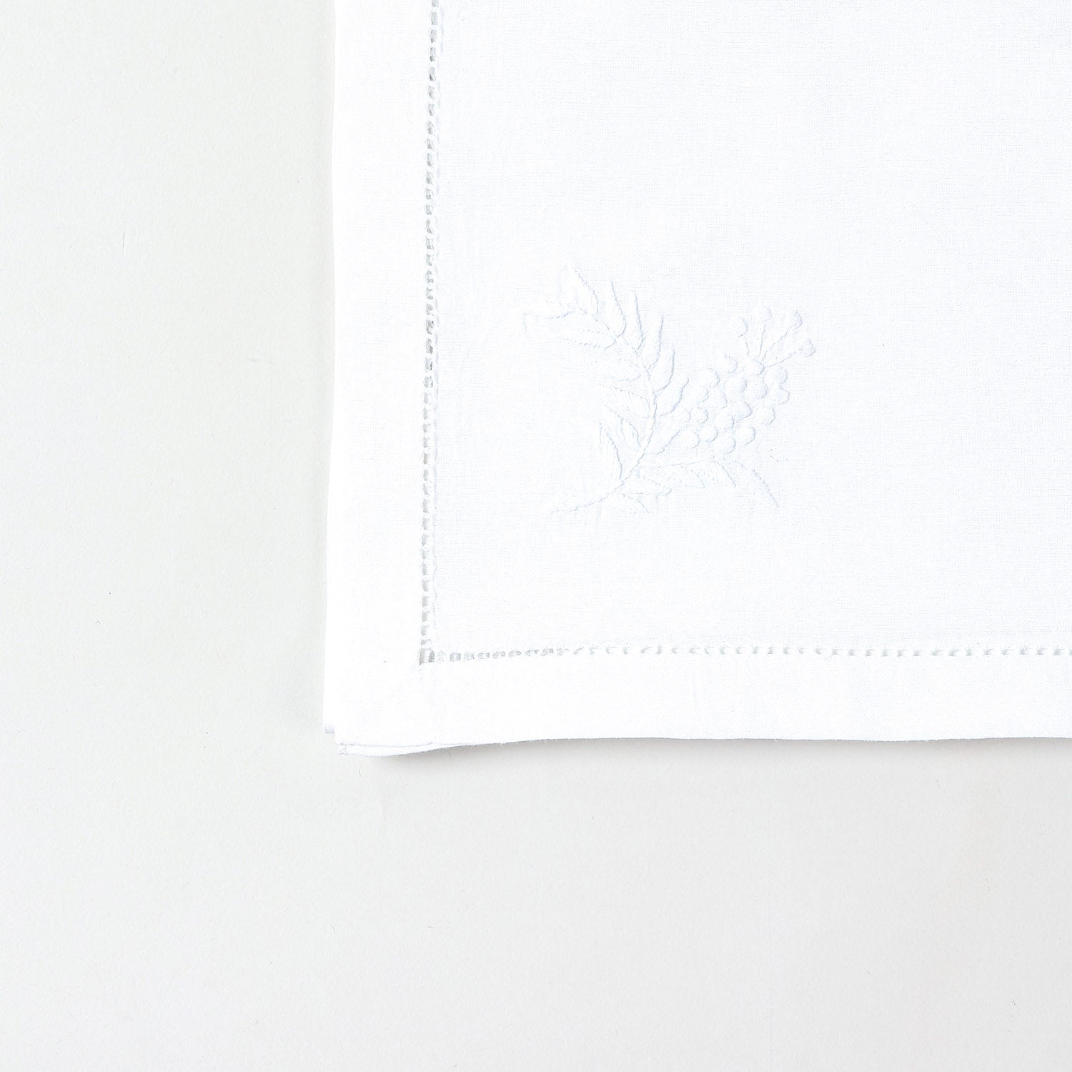 Detailed corner view of a handcrafted white cotton table runner featuring delicate wild floral chikankari embroidery
