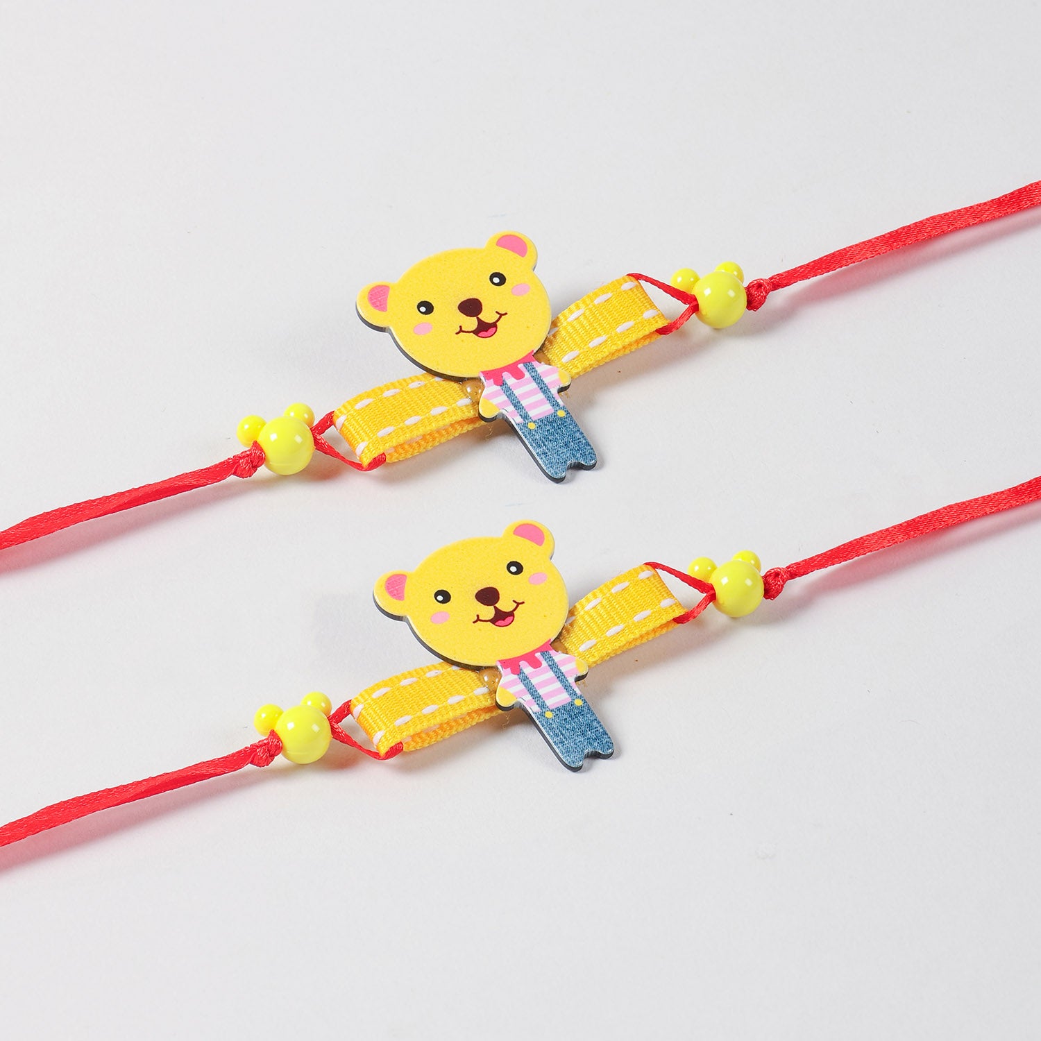 Close-up of the handmade yellow Cartoon Teddy Bear Wooden Kids Rakhi Set of 2, highlighting the wooden teddy design and red ribbon details.