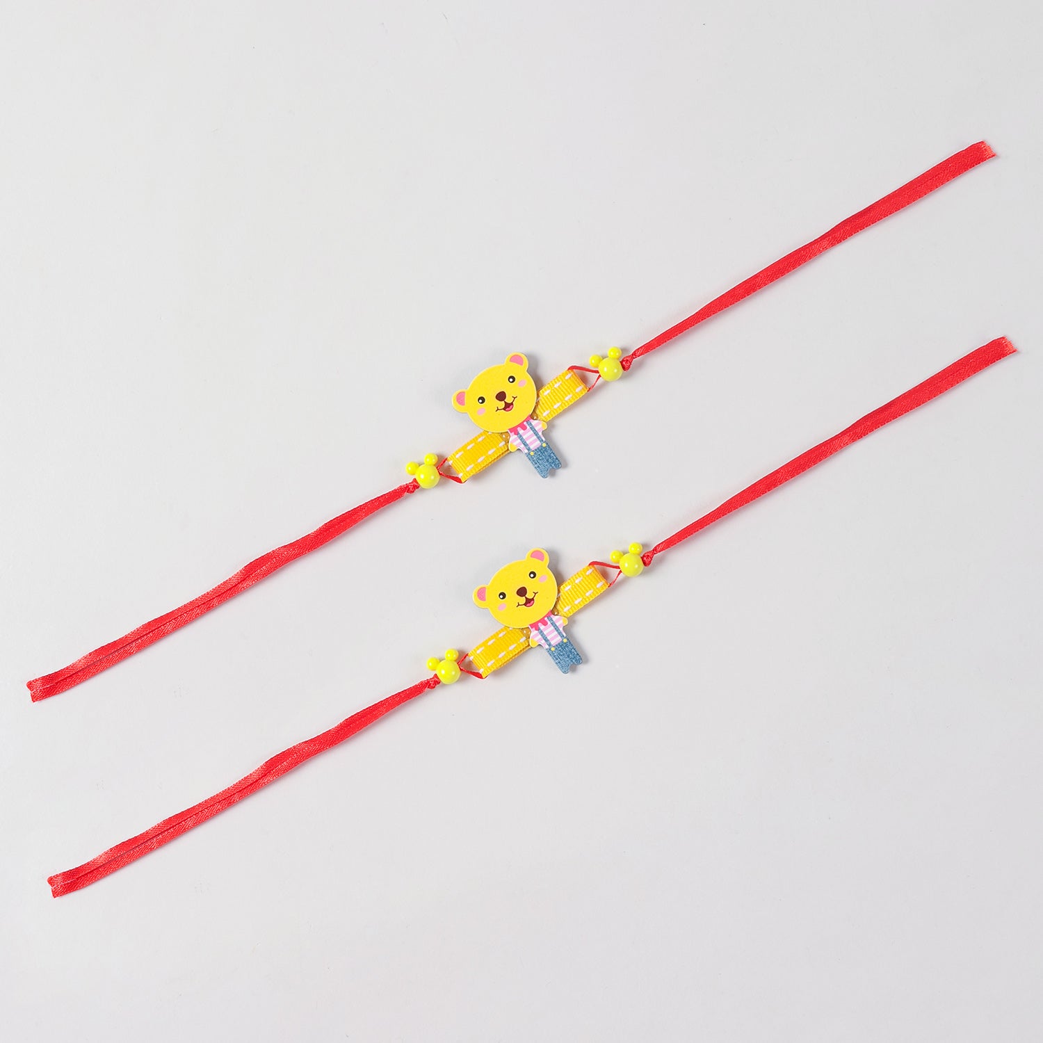 Full-length view of the yellow Cartoon Teddy Bear Wooden Kids Rakhi Set of 2, showing the complete red ribbon band and handcrafted teddy design.