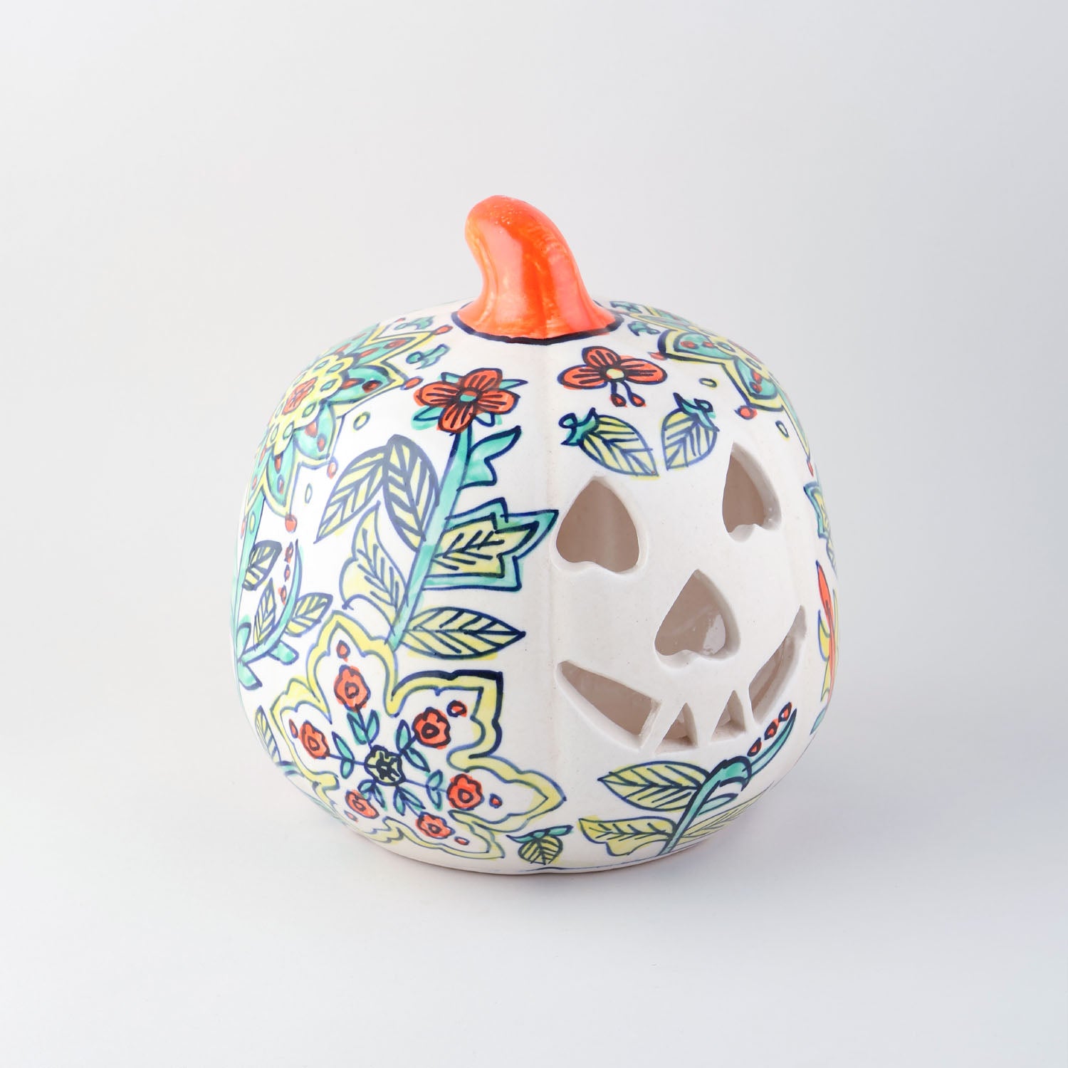 Side view of a hand-painted ceramic pumpkin t-light holder with decorative cutwork and floral patterns