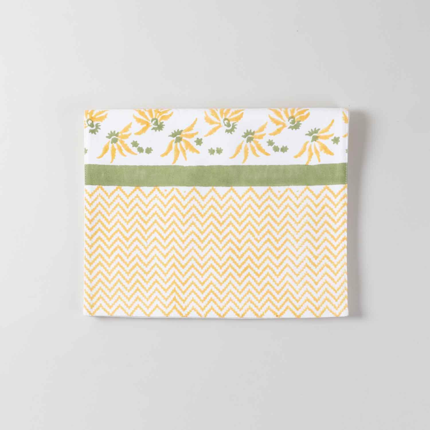 Folded cotton table runner featuring yellow floral block print motifs with a yellow chevron zigzag pattern  and a solid green line on  the edge