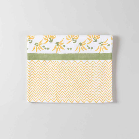 Folded cotton table runner featuring yellow floral block print motifs with a yellow chevron zigzag pattern  and a solid green line on  the edge