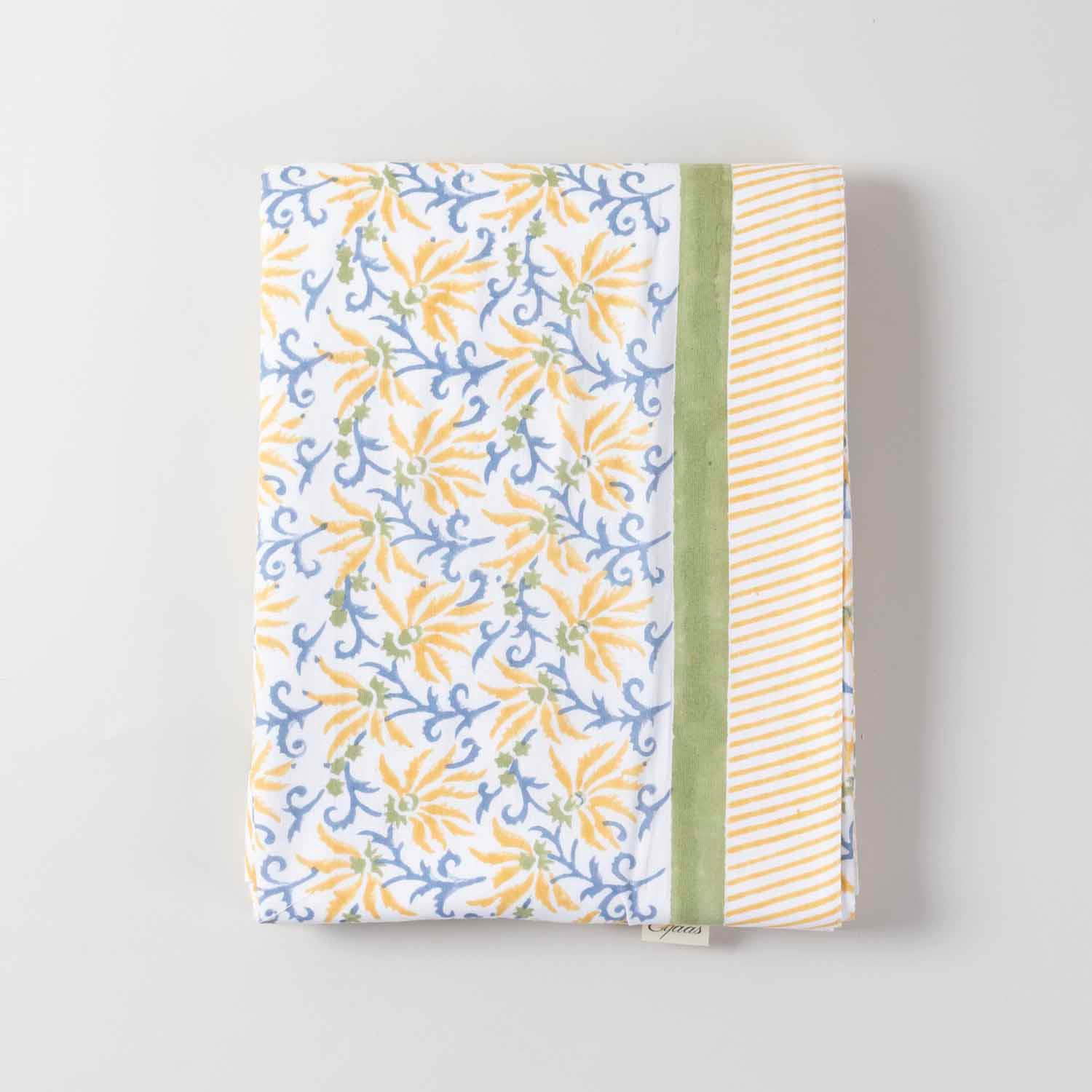 Folded high-angle view of a yellow lily hand-block printed cotton tablecloth displaying floral motifs and overall layout