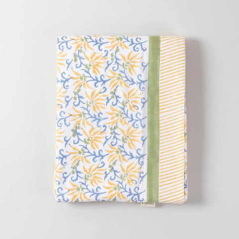 Folded high-angle view of a yellow lily hand-block printed cotton tablecloth displaying floral motifs and overall layout