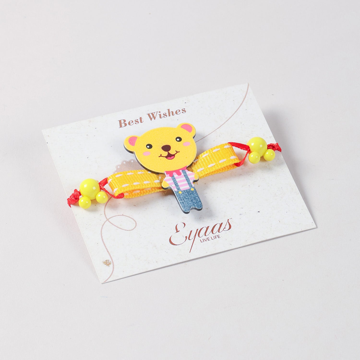 Angled view of the yellow Teddy Bear Wooden Kids Rakhi Set of 2 attached to a festive Best Wishes card, ready for Raksha Bandhan gifting