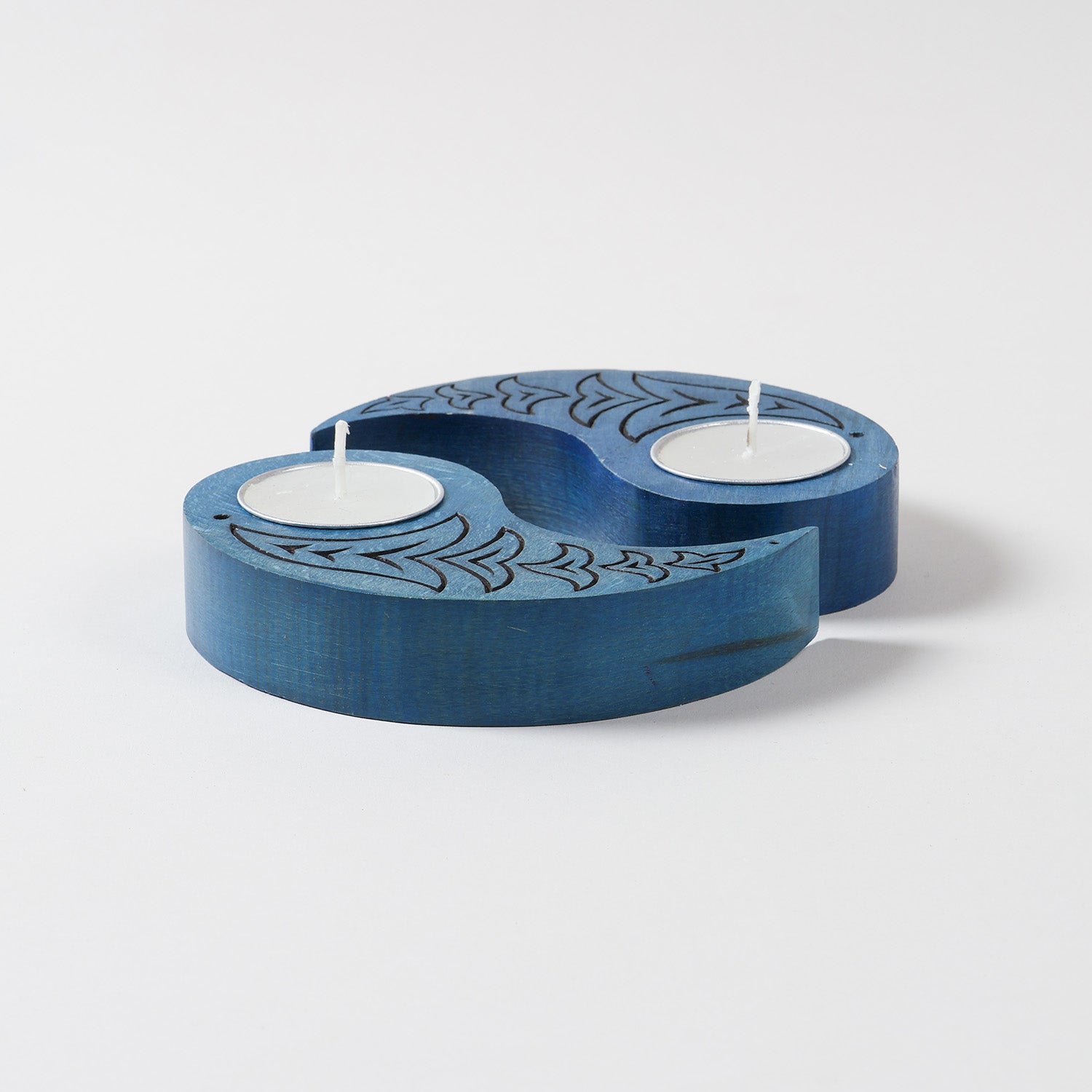 Side angled view of blue wooden tea light candle holders with Ying Yang bird carvings, displayed with unlit T-lights on a plain background