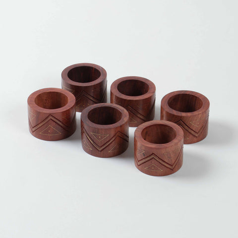 Angled view of a set of six wooden napkin rings featuring decorative zig-zag carving and brass inlay