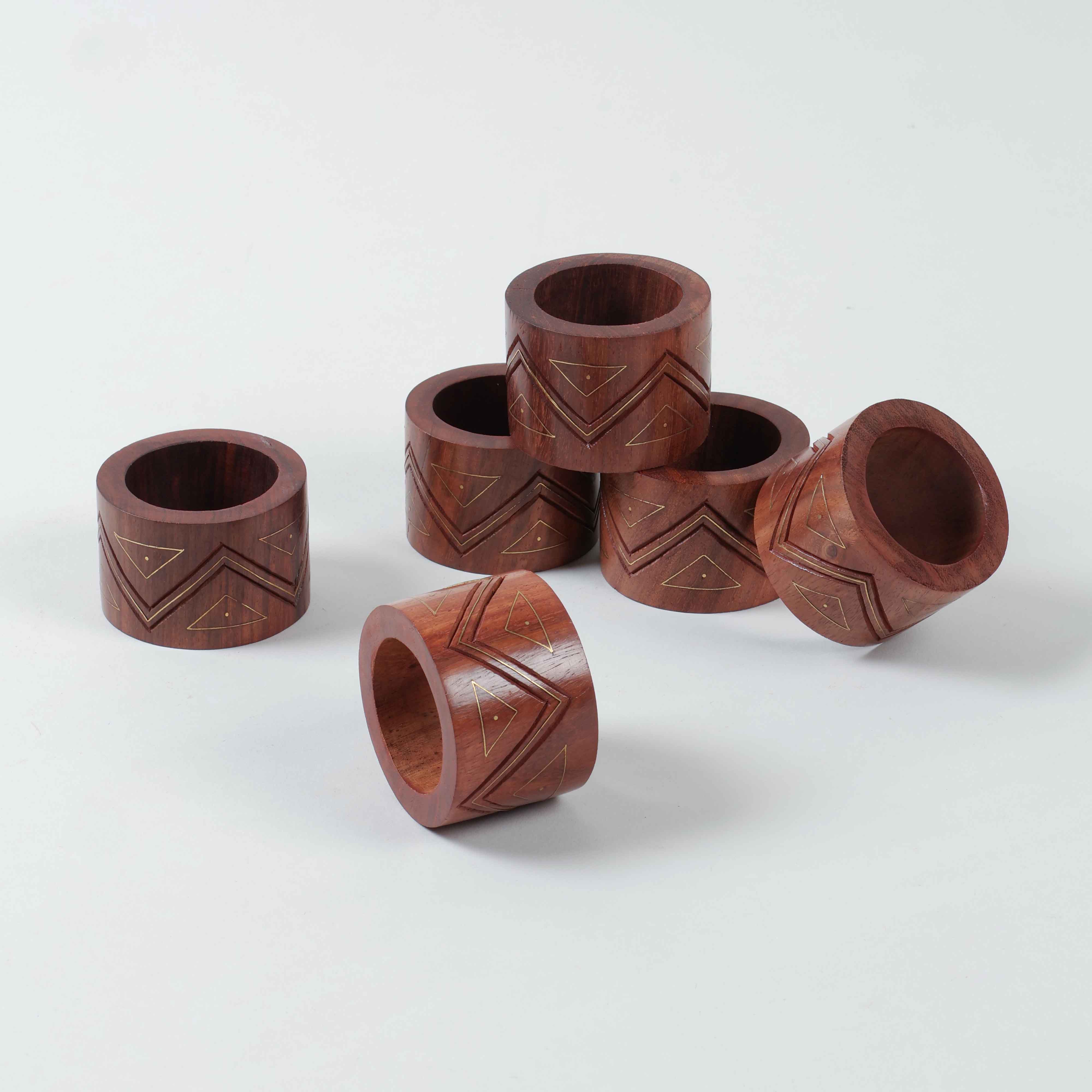 Side view of six wooden napkin holder rings stacked displaying hand carved patterns and brass accents